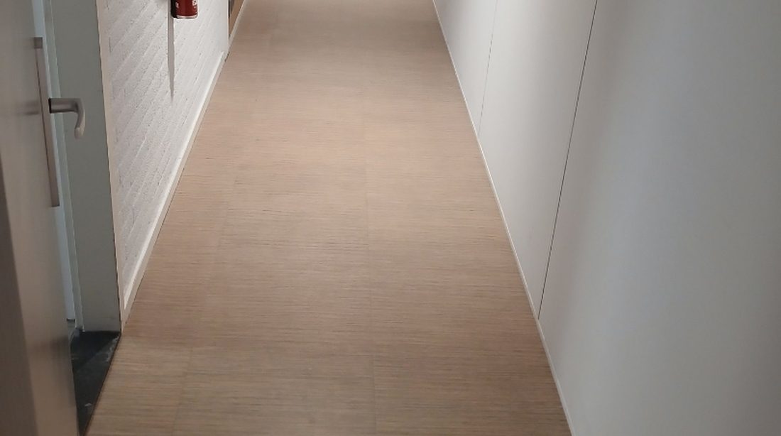 A long, empty office corridor lit by ceiling panels in the evening