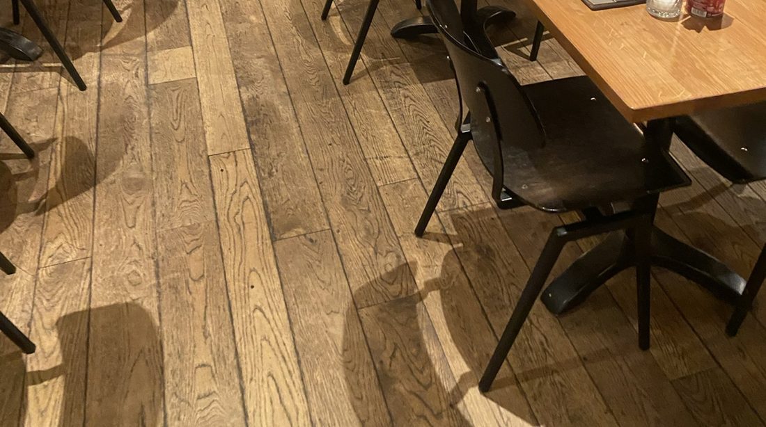 Een geoliede eiken plankenvloer onder de tafels van een restaurant