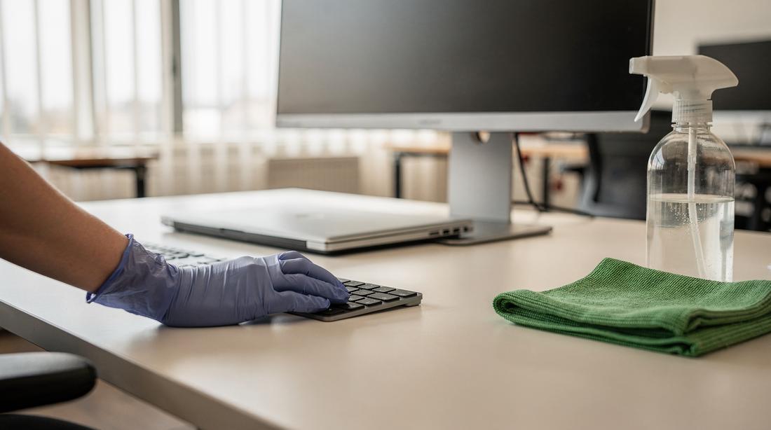 Bureau wordt gedesinfecteerd, toetsenbord en blad afgenomen rond een dichtgeklapte laptop