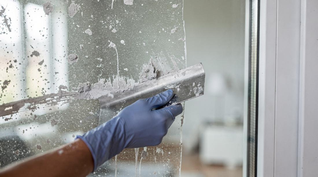 Paint spatter and adhesive being scraped off a new window pane, half the glass already clear