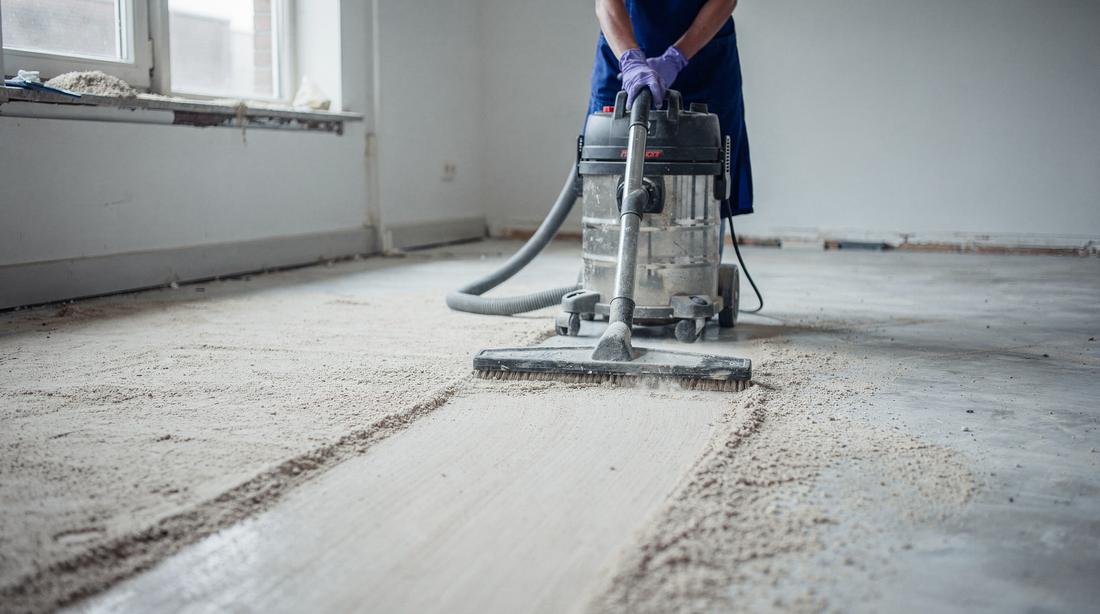 Industrial HEPA vacuum leaving a clean swept band through construction dust on a bare floor