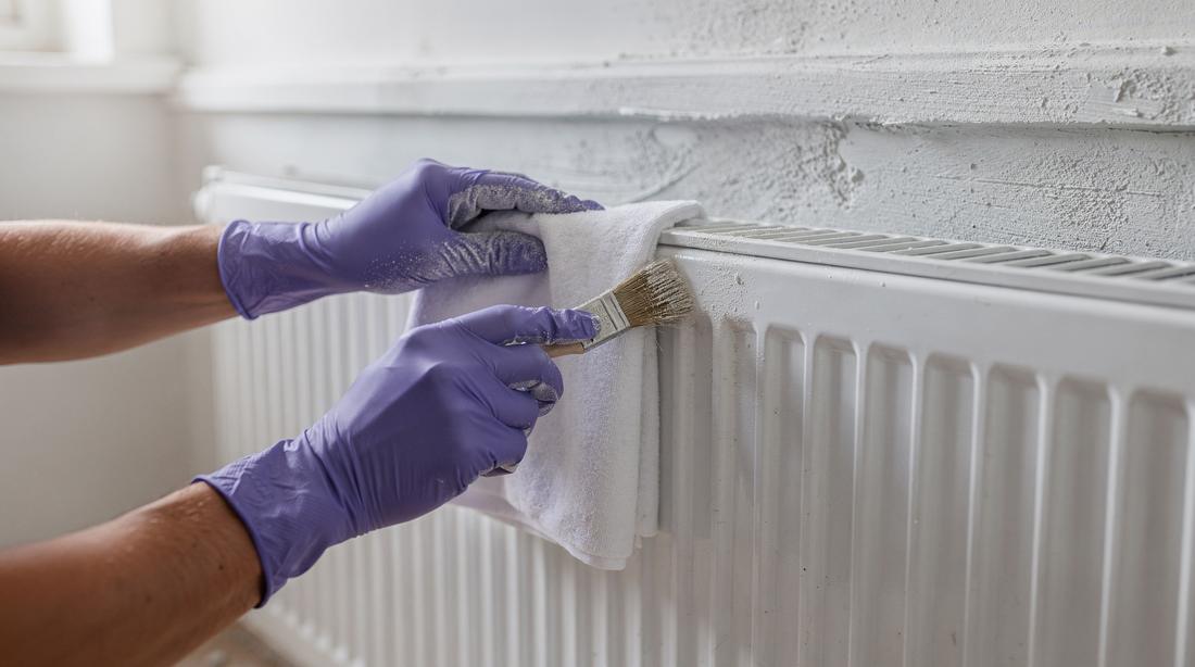 Radiator fins and new skirting being detailed with a narrow brush after plastering