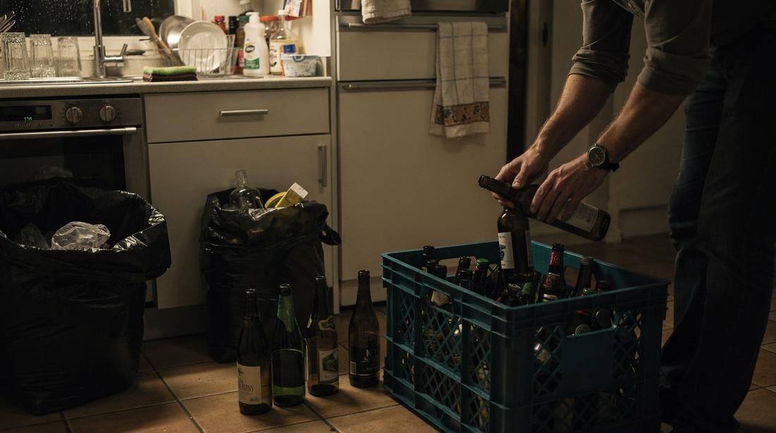 Lege flessen worden in een kratje gesorteerd op een Nederlandse keukenvloer, glaswerk opgestapeld bij de gootsteen