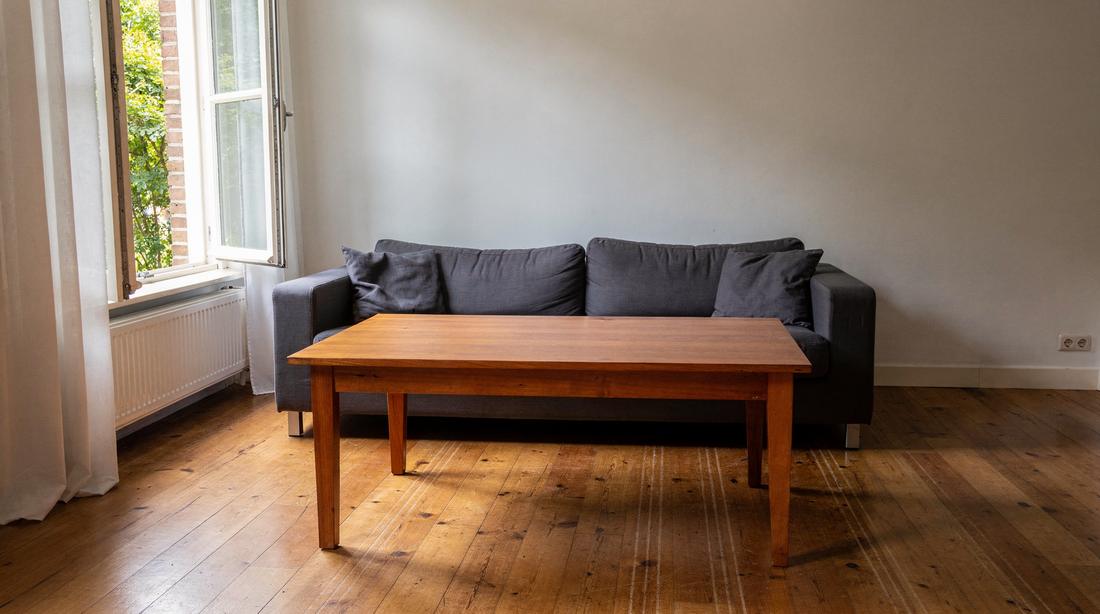 Dezelfde woonkamer opgeruimd en schoon: lege gepoetste tafel, rechte kussens, verse zuiglijnen op de vloer