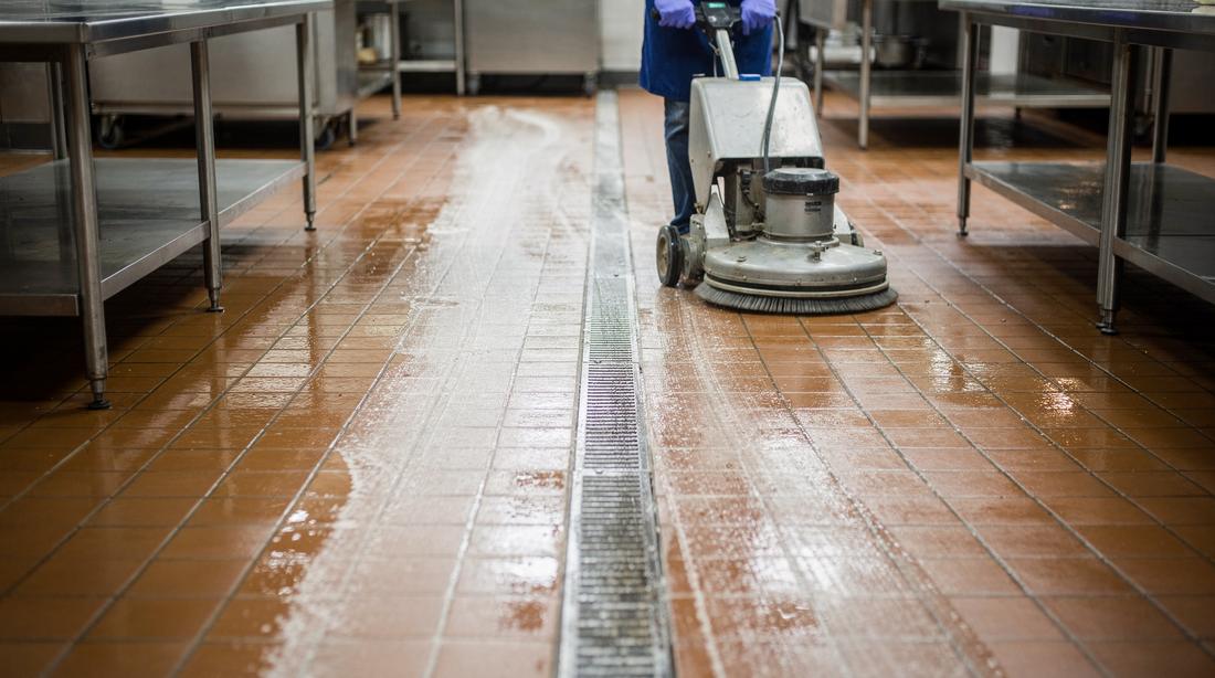 Plavuizen keukenvloer wordt machinaal geschrobd, voegen duidelijk lichter waar de machine is geweest