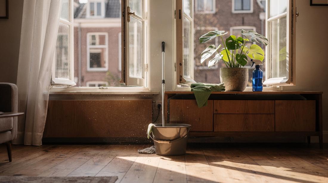 Sunlit Dutch living room mid spring-clean, sash windows open and a mop resting in a bucket