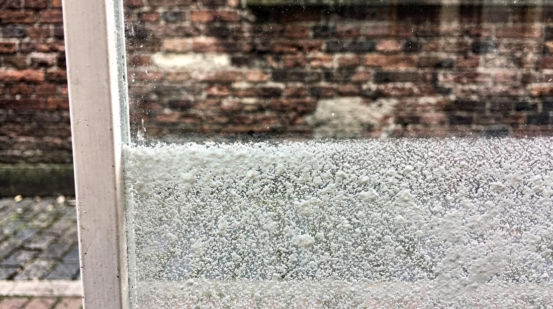 Ruit met opgedroogde kalkvlekken op de onderste helft en volkomen helder glas erboven
