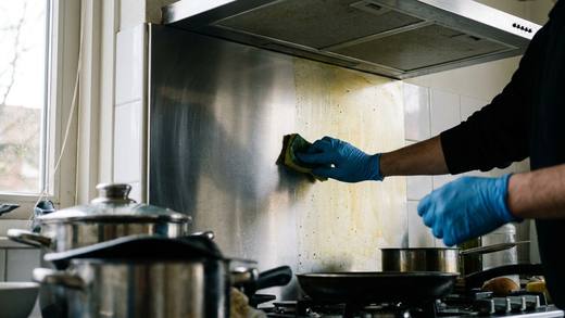 Handen met handschoenen ontvetten een afzuigkap, de helft glanst al