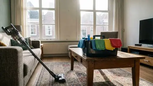 A tidy living room with a vacuum and a cleaning caddy
