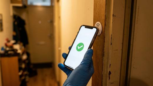 Hand met handschoen tikt een telefoon tegen de NFC-check-in-sticker naast een voordeur