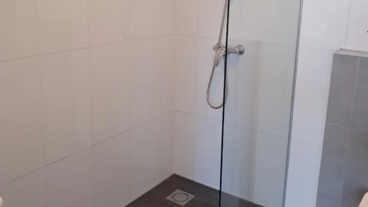 A walk-in shower with a glass screen and white tiles, cleaned after a move-out