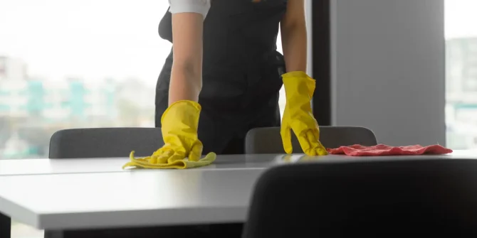 a woman wearing yellow gloves cleaning a table
